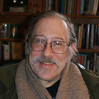 a man with a thick jacket, glasses, grey hair and grey facial hair smiles at the camera