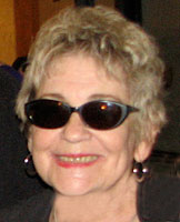 a woman with styled grey hair, earrings, and dark sunglasses smiles