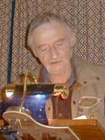 a man with a tan jacket and grey hair stands at a lectern